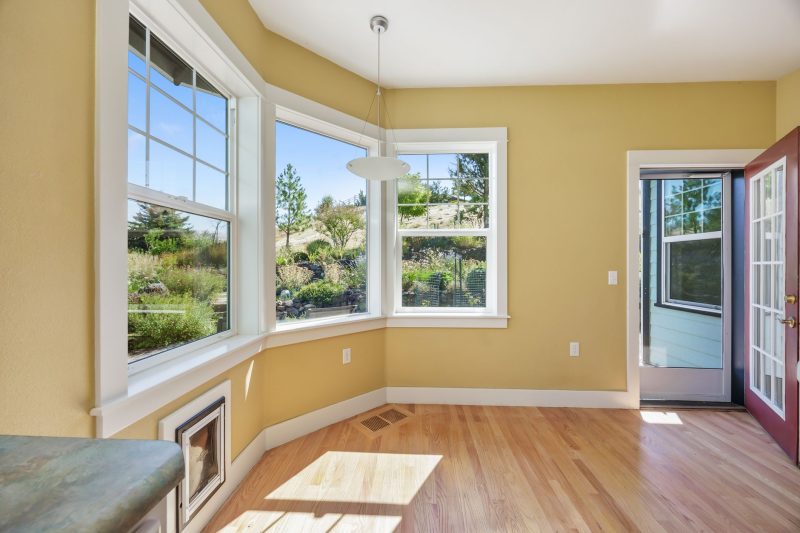 Spacious sunlit room with wooden floors and large windows offering views of a lush garden.