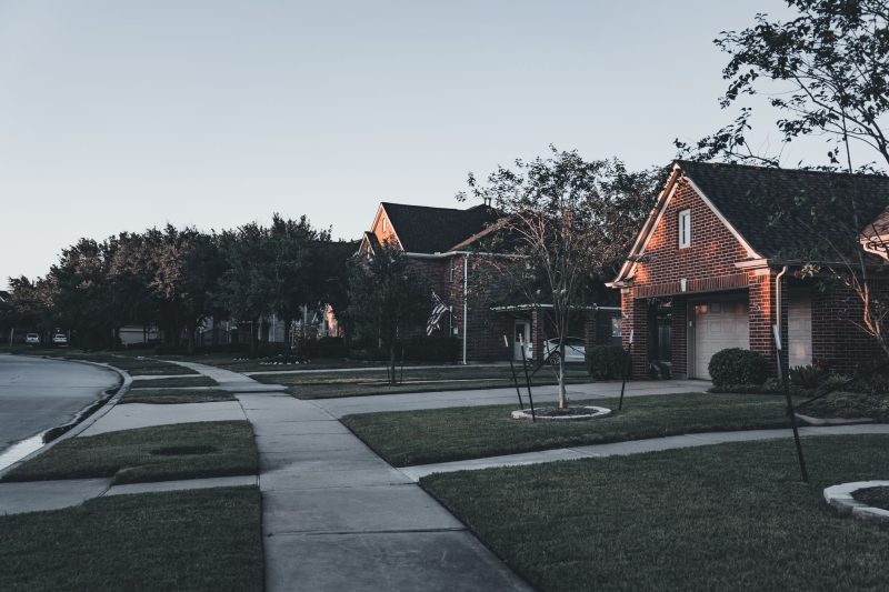 Serene suburban scene with brick houses and landscaped lawns, bathed in warm dusk light.