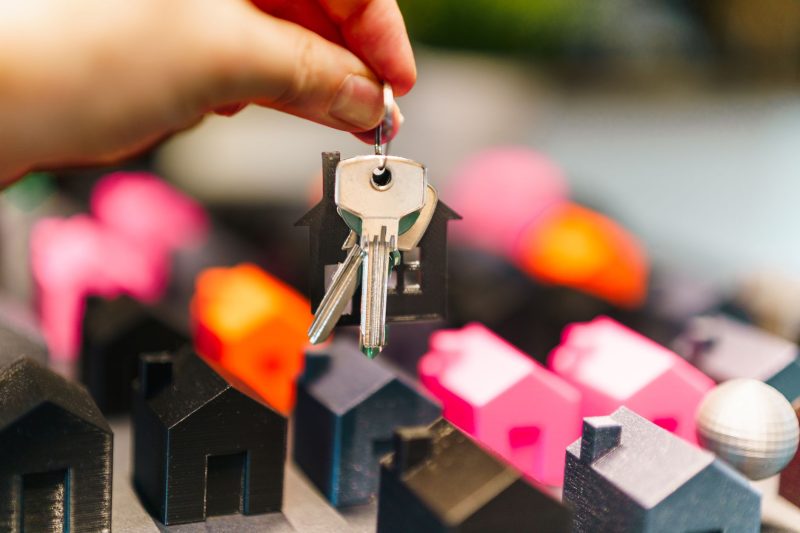 A hand holding a set of keys above colorful miniature houses.