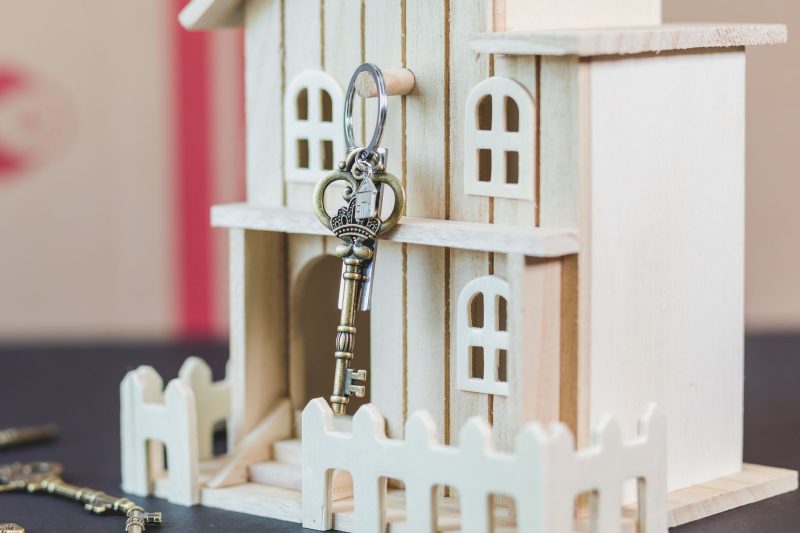 Miniature wooden house next to a vintage key on a light background.
