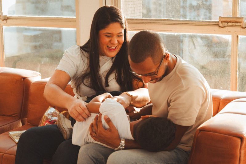Family bonding on a couch in a warm, sunlit living room with bright decor.